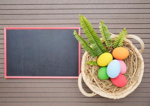 Colorful easter eggs in the basket and blackboard on wood background with space