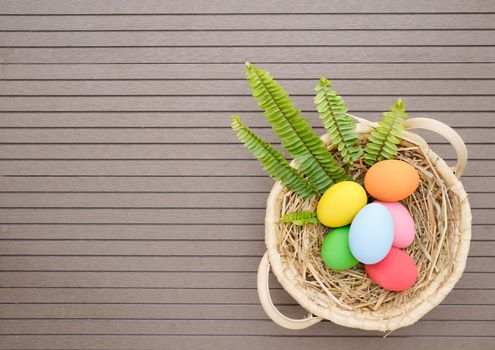 Colorful easter eggs in the basket on wood background with space