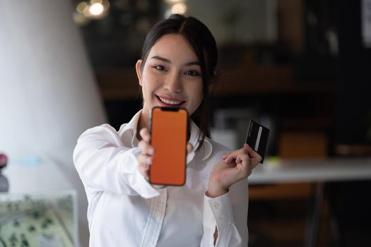 Portrait of smiling young woman show smartphone and credit card for shopping online at home