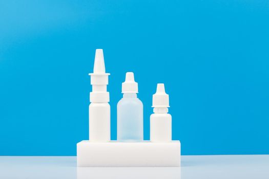 Three different nose sprays on white podium against blue background. Concept of medication for running nose or allergic rhinitis