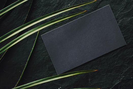 Black business card flatlay on dark stone background and green exotic leaf, luxury branding flat lay and brand identity design for mockups