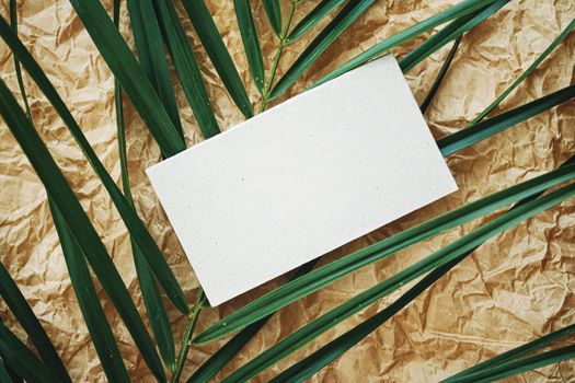 White business card flatlay on brown parchment paper background and green exotic leaf, luxury branding flat lay and brand identity design for mockups