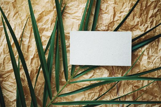 White business card flatlay on brown parchment paper background and green exotic leaf, luxury branding flat lay and brand identity design for mockups