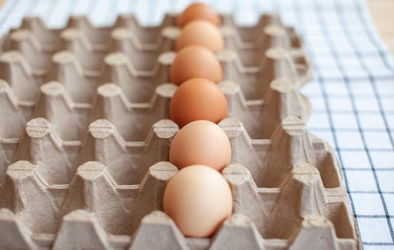 Several brown eggs lie in a row in a large cardboard bag, a chicken egg as a valuable nutritious product, a tray for carrying and storing fragile eggs