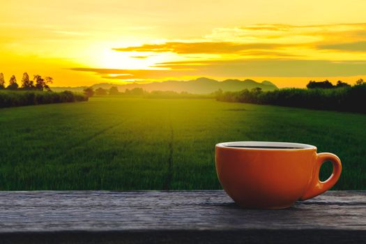 Hot coffee cup Ceramic brown glass placed on an outdoor old wood table. The background is a landscape of nature with mountains and rice field in the morning time