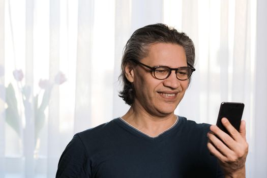 An adult gray-haired man with glasses is reading a text message on the phone. Close-up
