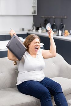 Fury, rage, anger with laptop in hand young overweight girl staying at home during quarantine. Self isolation as prevention. Work distantly concept. Facial expressions, emotions, feelings.