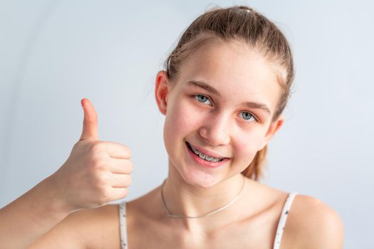 Teenage girl smiling in orthodontic brackets showing thumb up. Girl with braces on teeth. Orthodontic Treatment.