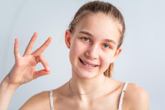 Teenage girl smiling in orthodontic brackets showing OK sign. Girl with braces on teeth. Orthodontic Treatment.