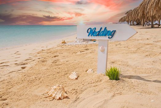 Closeup of wedding sign on tropical island sandy beach paradise with ocean in background and dramatic red sky