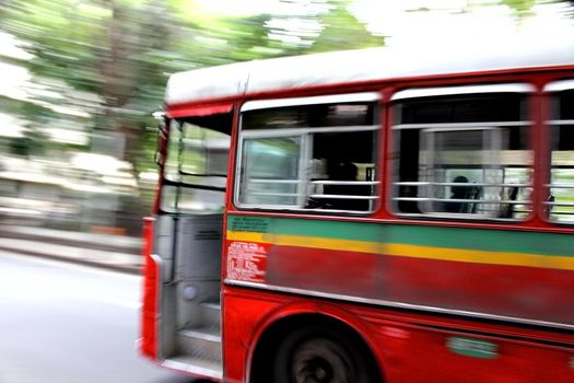 Beautiful Red Bus taking a sharp turn in full speed on the city street focused on Bus, the background is motion blurred, BEST Bus on Mumbai, India