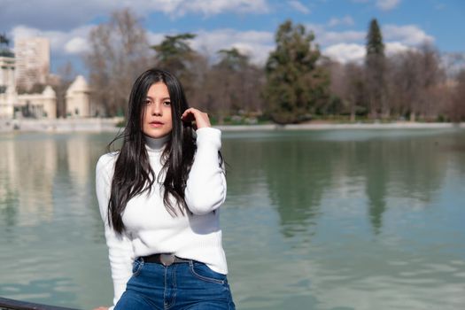 Young girl in blue jeans and white sweater with lake background