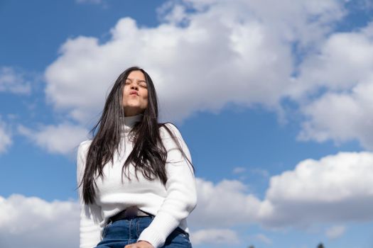 Young girl in blue jeans and white sweater with blue sky in the background