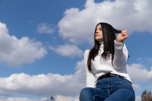 Young girl in blue jeans and white sweater with blue sky in the background