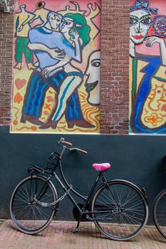 Classic-looking bicycle parked under modern painting of man and woman dancing. Bike leaning against brick wall with beautiful and colorful murals. Modern urban art and transportation