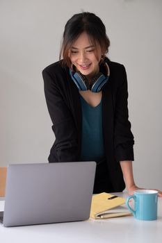 Portrait of asian woman studying online with laptop computer while standing at the table and notebook at home