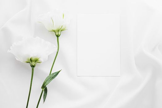 Wedding invitation and white rose flowers on silk fabric as bridal flatlay background, blank paper greeting card and holiday branding, flat lay design concept