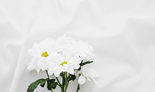 White daisy flowers on silk fabric as bridal flatlay background, wedding invitation and holiday branding, flat lay design concept