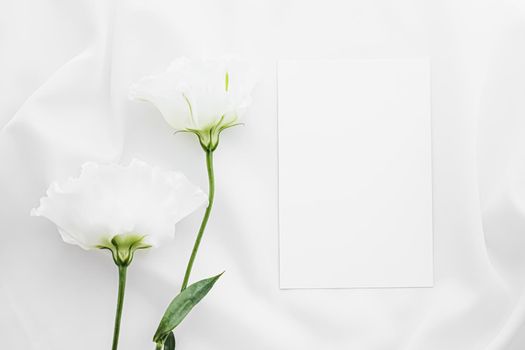 Wedding invitation and white rose flowers on silk fabric as bridal flatlay background, blank paper greeting card and holiday branding, flat lay design concept