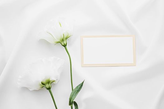 Wedding invitation or gift card and white rose flowers on silk fabric as bridal flatlay background, blank paper and holiday branding, flat lay design concept