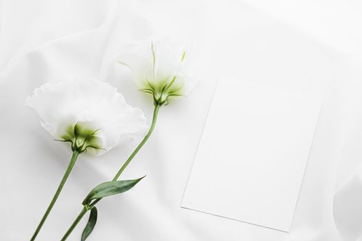 Wedding invitation and white rose flowers on silk fabric as bridal flatlay background, blank paper greeting card and holiday branding, flat lay design concept