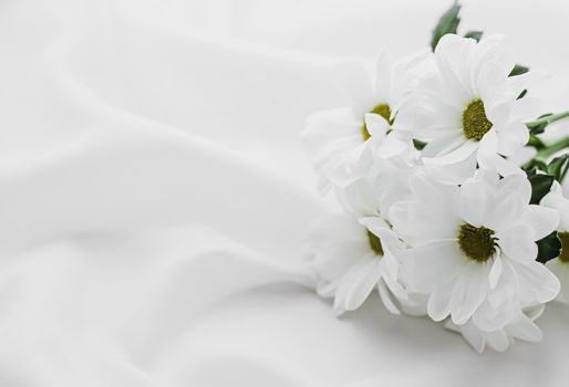 White daisy flowers on silk fabric as bridal flatlay background, wedding invitation and holiday branding, flat lay design concept