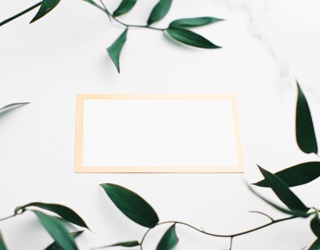 Blank white and gold card, green leaves on white background as botanical frame flatlay, wedding invitation and branding, flat lay design concept