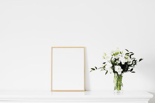 Golden vertical frame and bouquet of fresh flowers on white furniture, luxury home decor and design for mockup creations