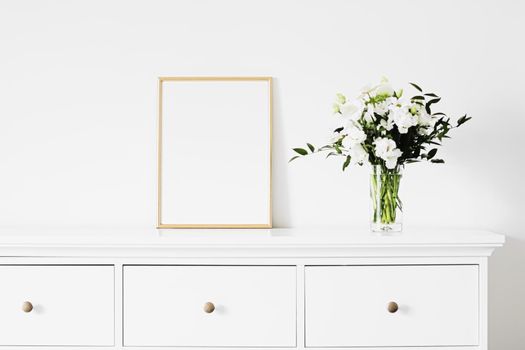 Golden vertical frame and bouquet of fresh flowers on white furniture, luxury home decor and design for mockup creations