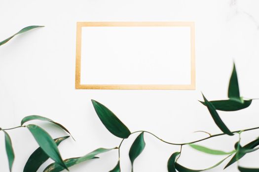 Blank white and gold card, green leaves on white background as botanical frame flatlay, wedding invitation and branding, flat lay design concept