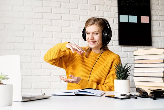 Distance learning. E-learning. Young smiling woman in yellow sweater and black headphones studying online using laptop talking in video chat