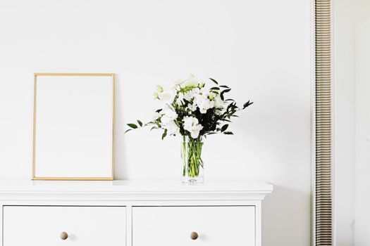 Golden vertical frame and bouquet of fresh flowers on white furniture, luxury home decor and design for mockup creations