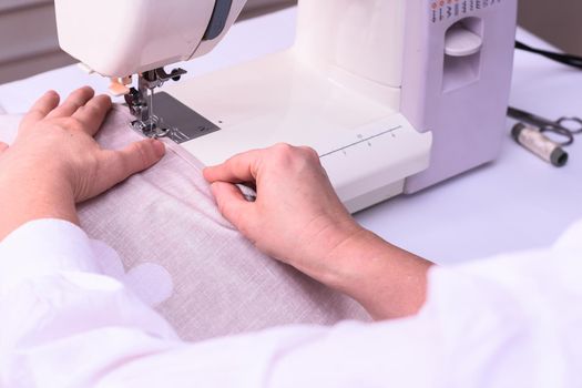 view of sewing process. Female hands stitching white fabric on machine. Seamstress hands holding textile for linen. Close up 