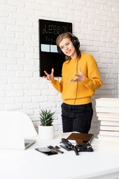 Distance learning. E-learning. Young smiling woman in yellow sweater and black headphones teaching online using video chat on laptop