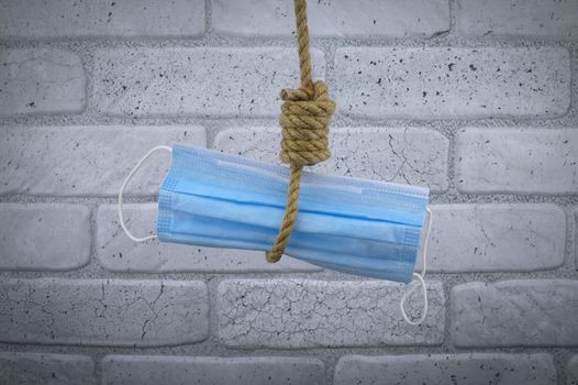 Rope noose around a protective surgical face mask, conceptual of death or mortality during the global Covid-19 or coronavirus pandemic against a brick wall background