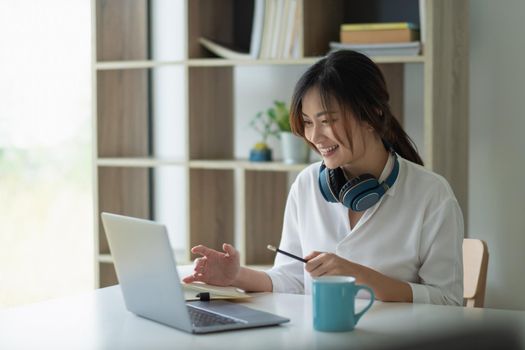 Portrait of a pretty young asian woman studying online with laptop computer while sitting at the table and notebook at home
