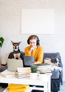 Distance learning. E-learning. Young smiling woman in yellow sweater and black headphones studying online using laptop, sitting on the couch at home