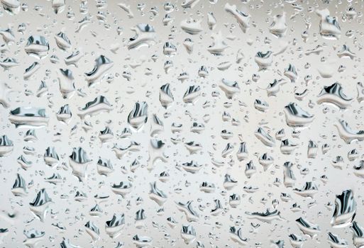 Rain droplets on glass with a white background. Seasonal and rain. Melancholy and mood.