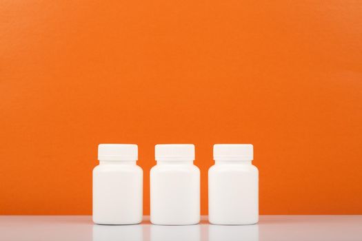 Three white unbranded medication bottles in a row against orange background with copy space. Concept of vitamin C, healthcare and wellness