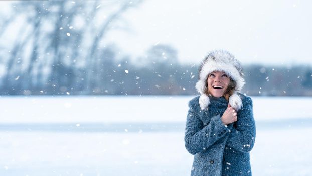 Young attractive woman happy with the falling snow in winter nature.