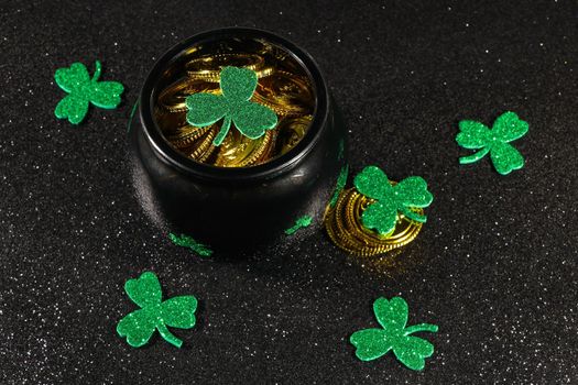 St Patrick's day pot of gold coins with shamrock clover leaves on textured black