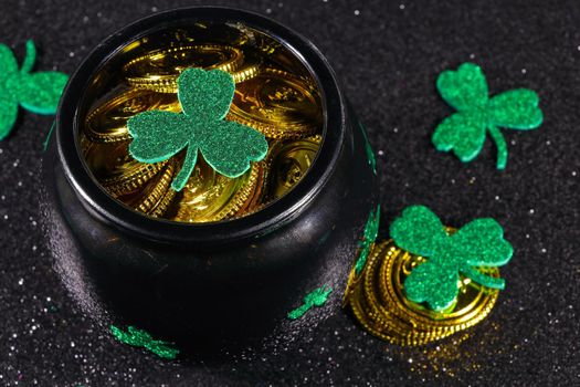 St Patrick's day coin filled pot of gold with shamrocks on textured black