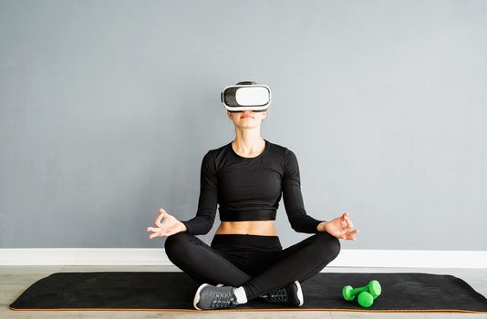 Fitness, sport and technology. Young athletic woman wearing virtual reality glasses doing yoga on fitness mat