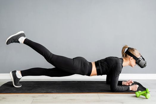Fitness, sport and technology. Young athletic woman wearing virtual reality glasses doingplank at blue background