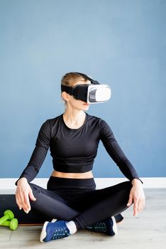 Fitness, sport and technology. Young athletic woman wearing virtual reality glasses sitting on fitness mat