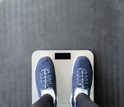 Dieting and weight loss. Top view of female feet in sport shoes standing on scales