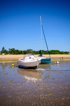 a sailing boat and a motorboat laying on the beach at lowtide on a sunny summertime on the Isle of île de re in the Charente-Maritime in France