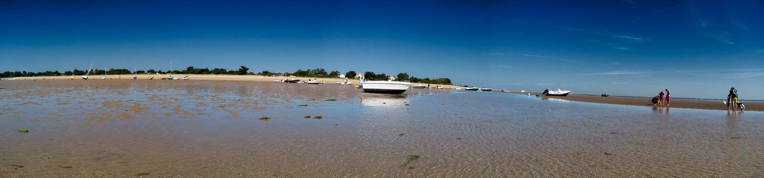 Panorama of people looking for crustaceans at low tide in Les Portes-en-Ré on the isle of ile de re in France and some boats laying on the sand.