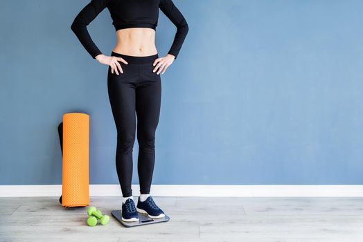 Dieting and weight loss. Woman in black sport clothes standing on scales