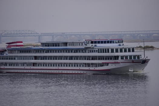 The passenger motor ship ruristic three-deck goes along the river, in the background is a large brid. High quality photo